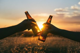 friends-toasting-with-beer-bottles-in-meadow-at-sunset